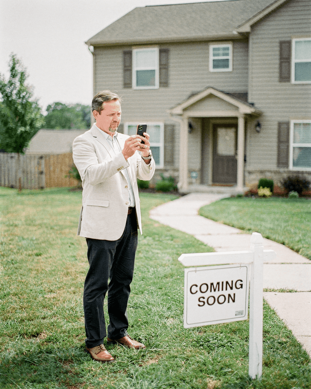 Realtor photographing a house behind a Coming Soon yard sign
