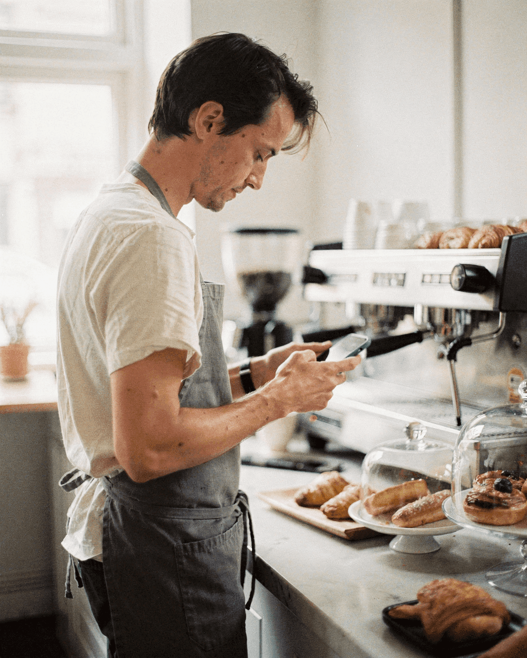 Coffee shop owner typing a caption on his phone behind the counter