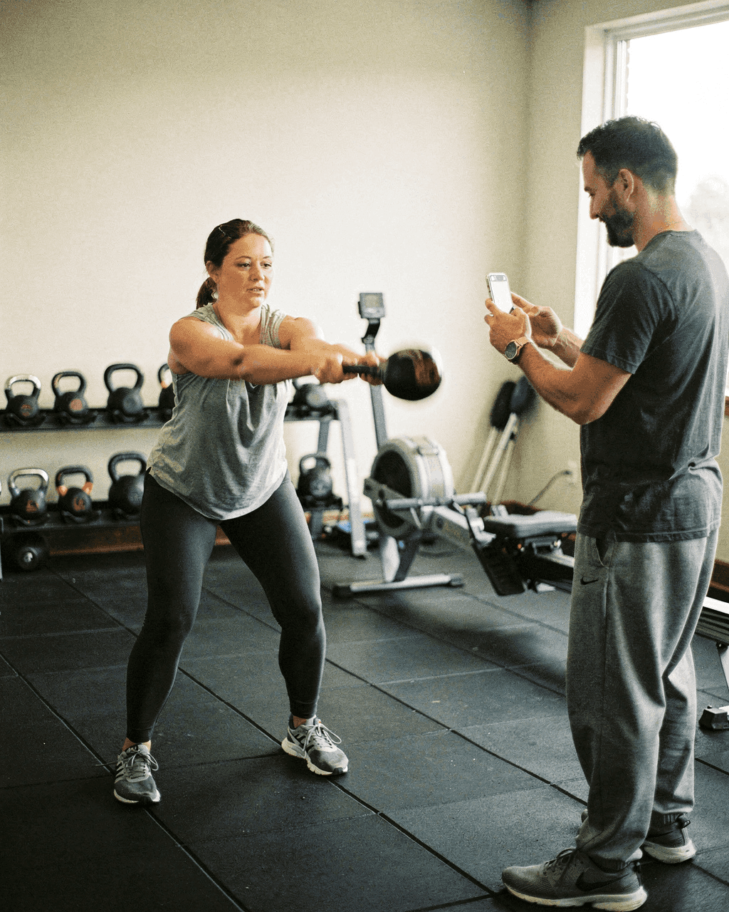 Gym coach filming a client's kettlebell swing on his phone