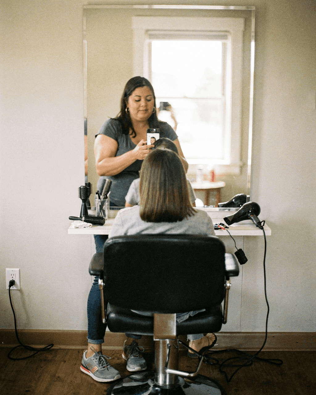 Stylist taking a phone photo of a client's finished haircut in the salon chair